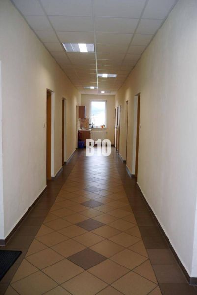 Chodba v kanceláři s dlaždicemi, dveřmi a oknem, interiér osvětlený umělým světlem.