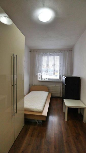Jednoduše zařízený pokoj s jedním lůžkem a podlahou s dřevěným dekorem ve 4pokojovém bytě.