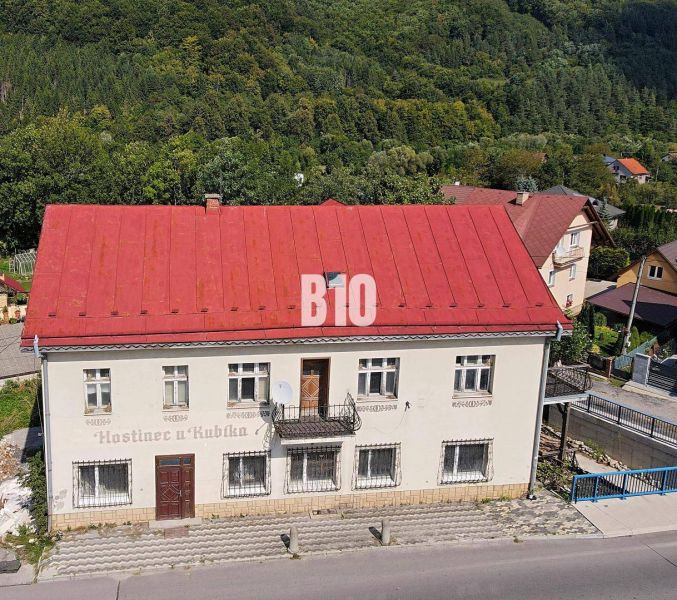 Budova v Belej s červenou střechou, obklopená zelení a cestou v popředí.