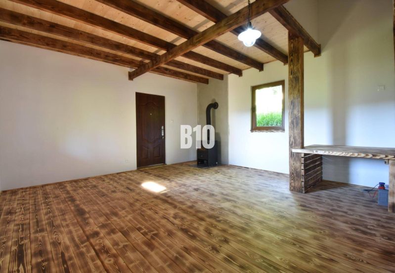 Interiér chaty s dřevěným stropem, podlahou a kamny.