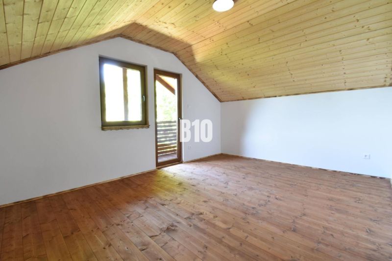Podkrovní prostory chaty s dřevěnou podlahou a stropem, okno a dveře na terasu.