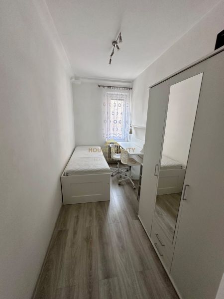 Jednoduchý pokoj s postelí, skříní a stolem, podlaha s dřevěným dekorem.