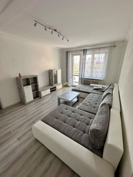 Obývací pokoj v 3-pokojovém bytě s podlahou s dřevěným dekorem, velkou sedačkou a televizí.