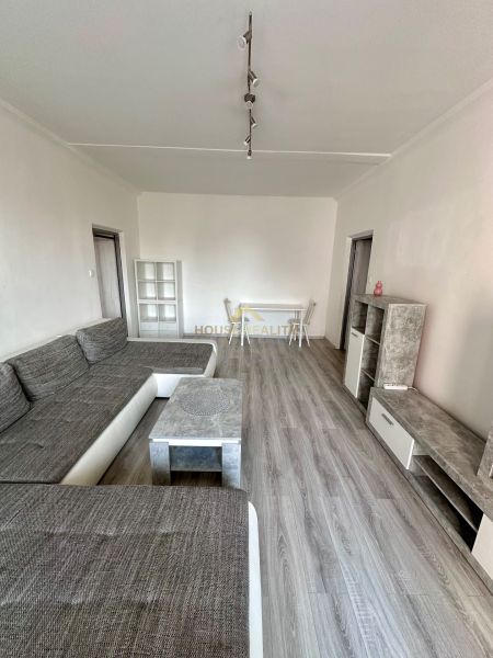 Obývací pokoj s podlahou s dřevěným dekorem a šedou sedací soupravou ve 3-pokojovém bytě.