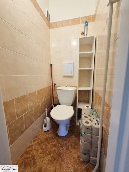 Koupelna s toaletou, bílými kachličkami a regálem ve 3-pokojovém bytě.