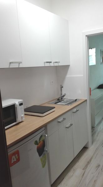 Kuchyňský kout v garsonce se skříňkami, mikrovlnkou a podlahou s dřevěným dekorem.
