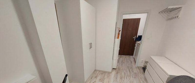 Útulná garsonka s bílým nábytkem a podlahou s dřevěným dekorem.