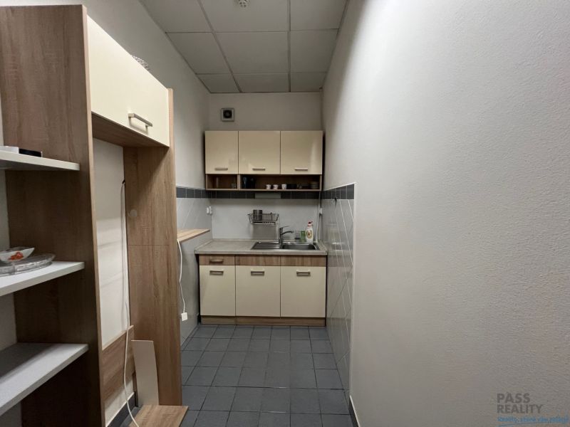 Úzká kuchyňka v kancelářích s jídelním koutkem a regály na skladování.
