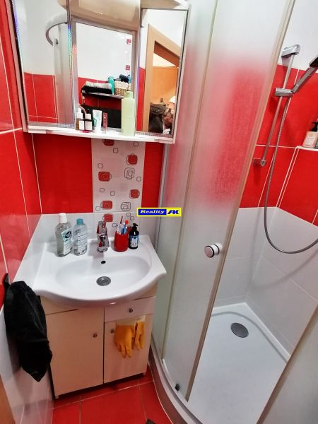 Koupelna s červenými obklady, sprchovým koutem a umyvadlem v 1-pokojovém bytě.