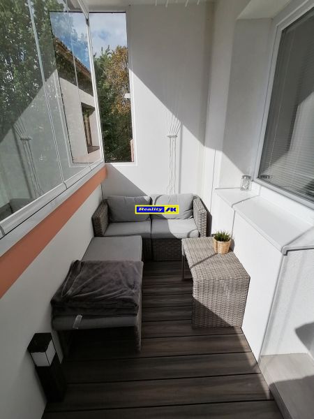Prosklený balkon s ratanovým nábytkem a podlahou s dřevěným dekorem v 1-pokojovém bytě.