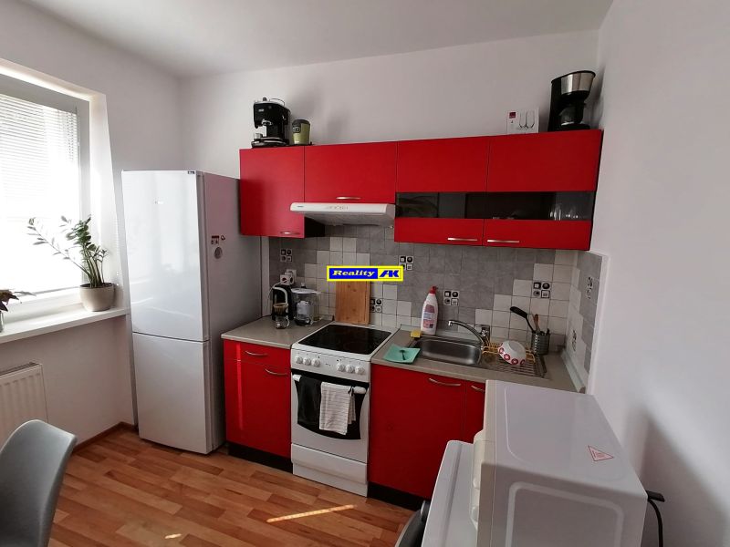 Kuchyně s červenými skříňkami a podlahou s dřevěným dekorem v 1-pokojovém bytě.