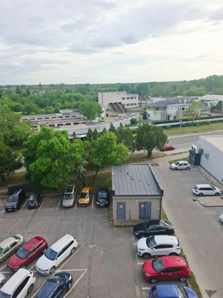 Parkoviště s auty, zelení a budovami v Nových Zámcích na ulici Nábrežná.