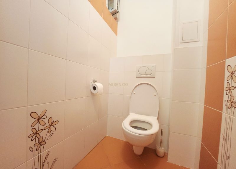 Toaleta s bílými obkladačkami a oranžovou dlažbou v 3-pokojovém bytě.
