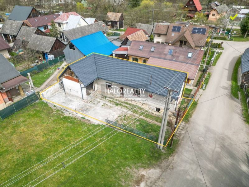 Rodinný dům ve Stupném s nízkým modrým střešním profilem, obklopený sousedními budovami.