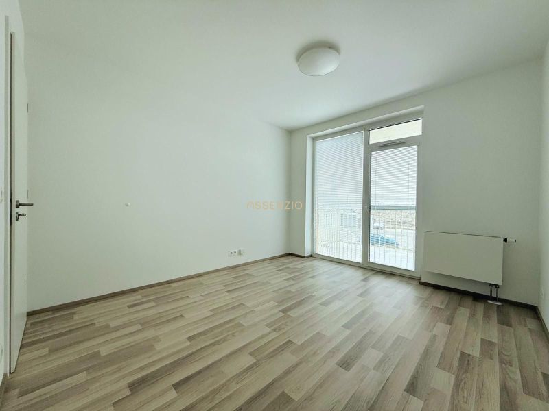 Pokoj v 2-pokojovém bytě s podlahou s dřevěným dekorem a vstupem na balkon.