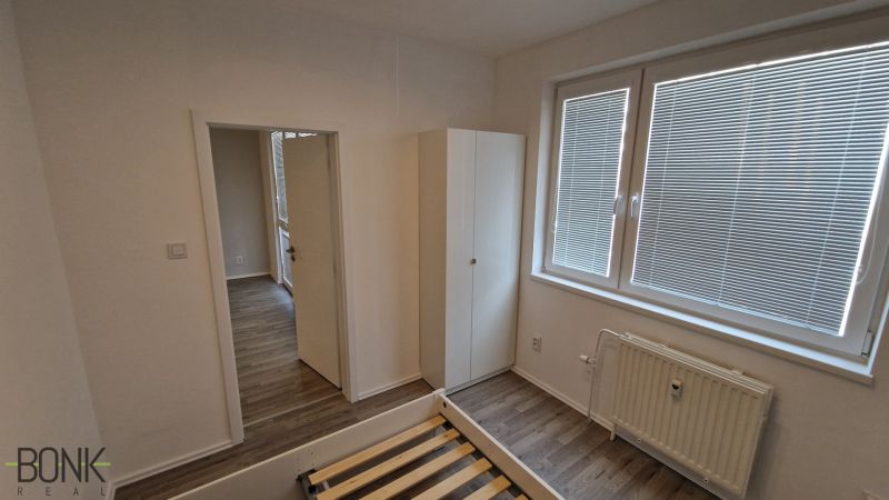 Ložnice v 2-pokojovém bytě s bílými stěnami a podlahou s dřevěným dekorem.