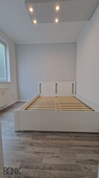 Manželská postel v pokoji s podlahou s dřevěným dekorem a stropním osvětlením.