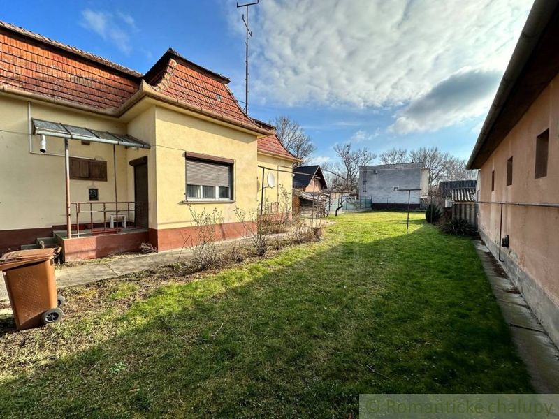Rodinný dům v Kolárově se zahradou, trávníkem a přístřeškem blízko vedlejší budovy.