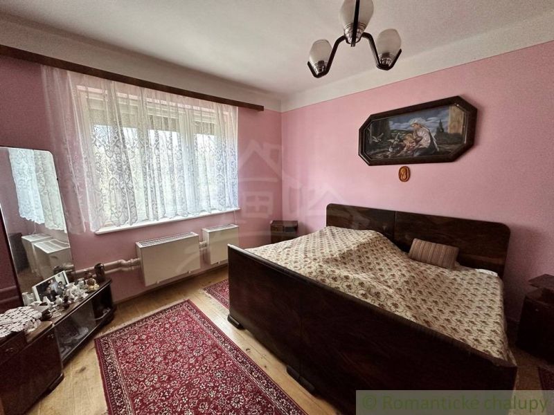 Ložnice s manželskou postelí, podlahou s dřevěným dekorem a růžovými stěnami v rodinném domě.
