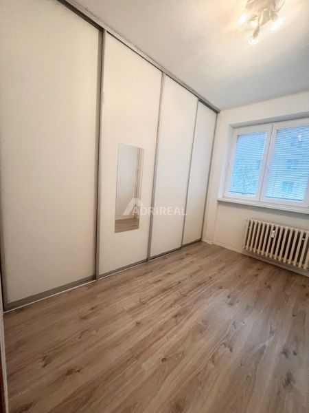 Pokoj ve 3-pokojovém bytě s bílou skříní a podlahou s dřevěným dekorem.