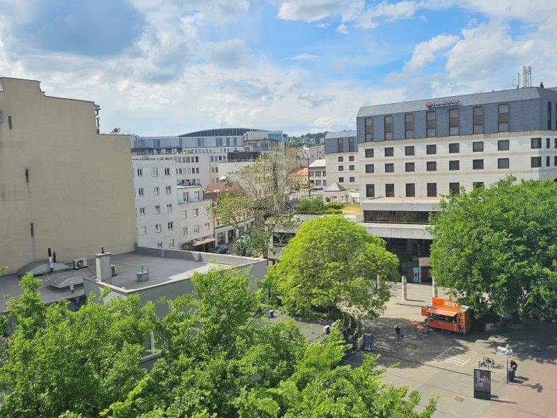 Pohled na Poštovní ulici v Bratislavě - Starém Městě se zelení a budovami.