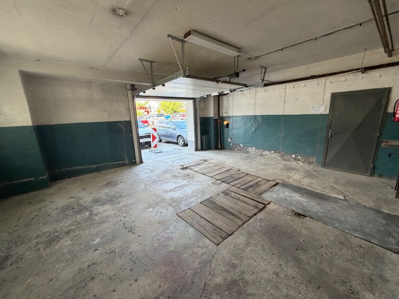 V garáži s otevřenými dveřmi, betonová podlaha. Bez auta.