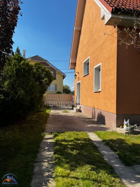Rodinný dům v Čalovci s oranžovou fasádou, trávníkem a zpevněnou příjezdovou cestou.