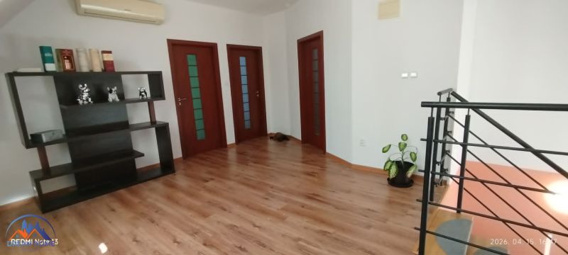Interiér rodinného domu s podlahou s dřevěným dekorem, poličkou a rostlinou.