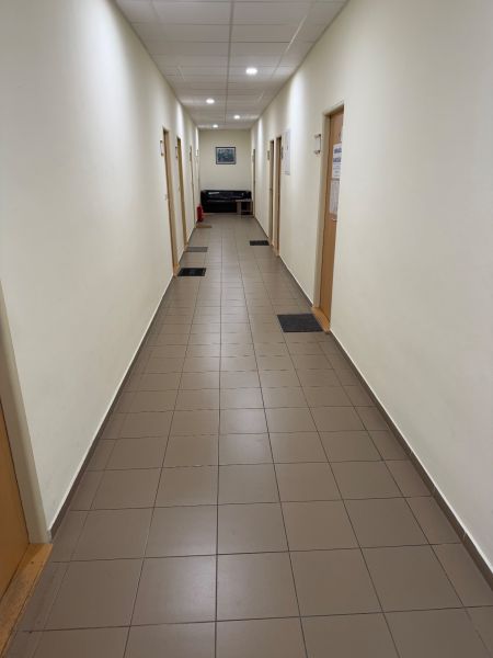 Úzká chodba v kancelářích s dlažbou, dveřmi a pohovkou na konci.