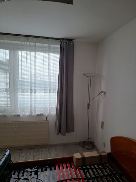 Pokoj s postelí, okny a podlahou s dřevěným dekorem ve 2pokojovém bytě.