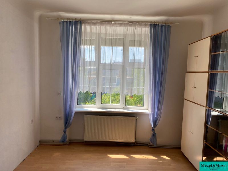 Pokoj se skříňkou, oknem a závěsy v 2-pokojovém bytě, podlaha s dřevěným dekorem.