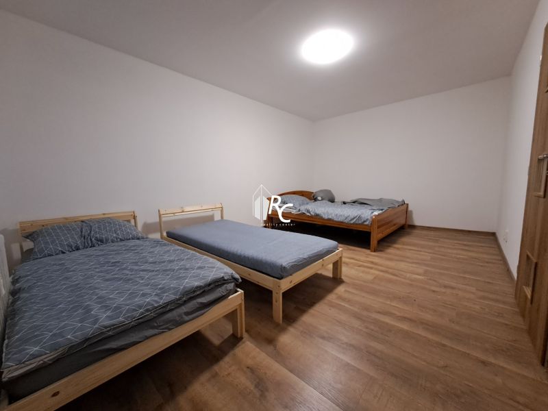 Ložnice se třemi postelemi a podlahou s dřevěným dekorem v 1-pokojovém bytě.