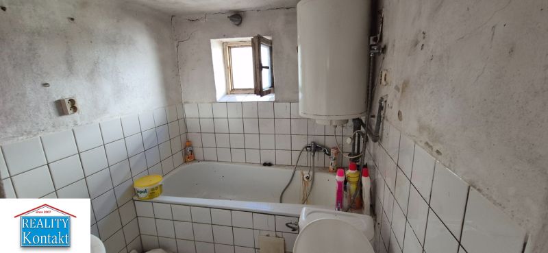 Koupelna v rodinném domě s obklady, vanou a bojlerem.