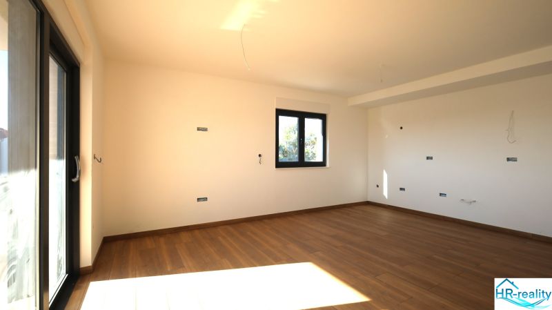 Prostorná místnost s velkým oknem a podlahou s dřevěným dekorem v Rekreačním apartmánu.