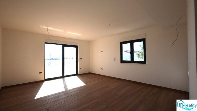 Interiér rekreačního apartmánu s velkými okny a podlahou s dřevěným dekorem.