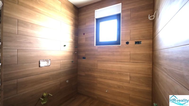 Rekreační apartmán s obklady v dřevěném dekoru a malým oknem.