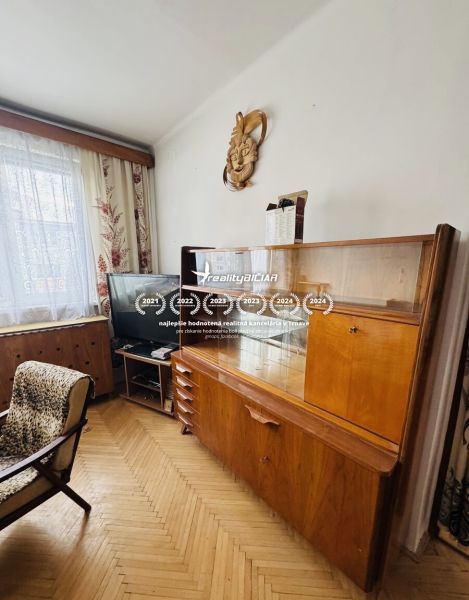 Pohled do obývacího pokoje s retro nábytkem a podlahou s dřevěným dekorem ve 3-pokojovém bytě.