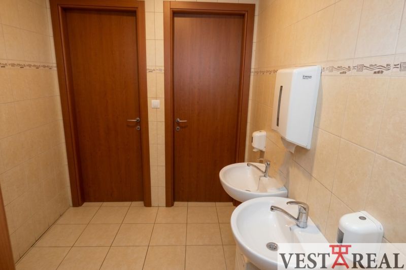 Toaleta v kancelářích se dvěma umyvadly a dveřmi, obložená keramickými dlaždicemi.