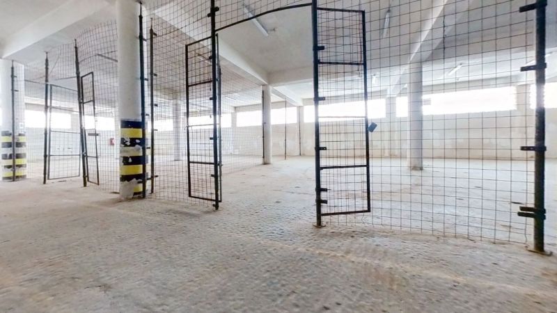 Oplocený interiér skladu a haly s otevřenými branami a světlými stěnami.