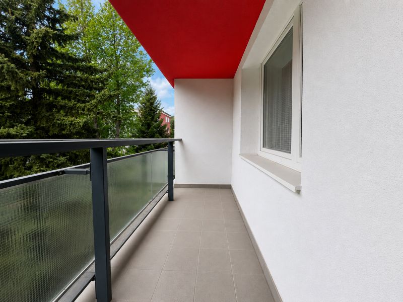 Balkon z 2pokojového bytu s červeným stropem a zábradlím se sklem.