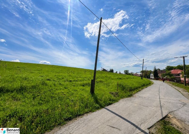Cesta vedoucí podél zelených pozemků k bydlení ve Finticích pod modrou oblohou.