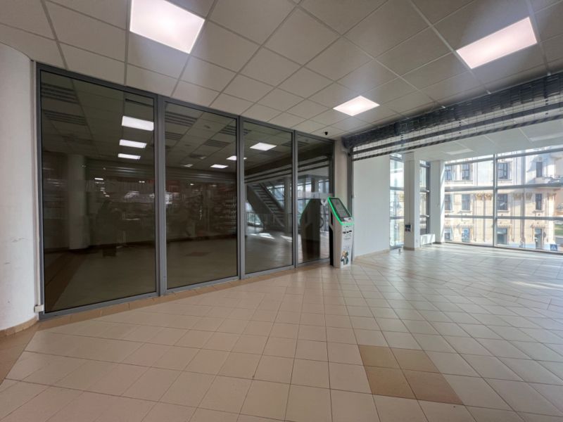 Prosklené obchodní prostory s dlažbou a bankomatem, interiér s velkými okny.