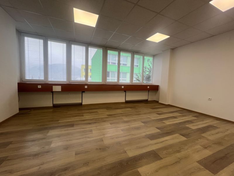 Prázdná kancelář s podlahou s dřevěným dekorem a velkými okny.