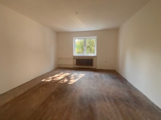 Prostorný pokoj v rodinném domě s podlahou s dřevěným dekorem a velkým oknem.