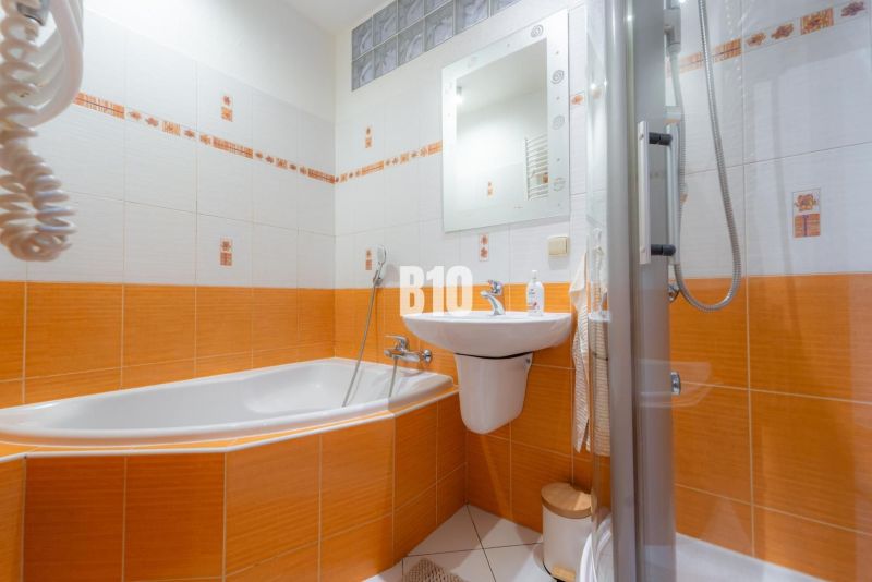 Koupelna v 2-pokojovém bytě s dominantními oranžovými obklady a vanou.