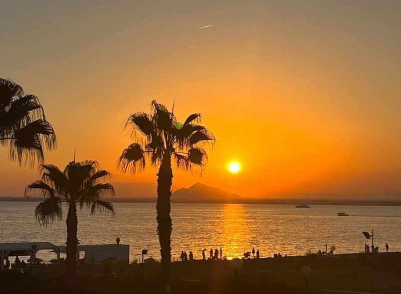Západ slunce s palmami a mořem v La Manga del Mar Menor, Španělsko.