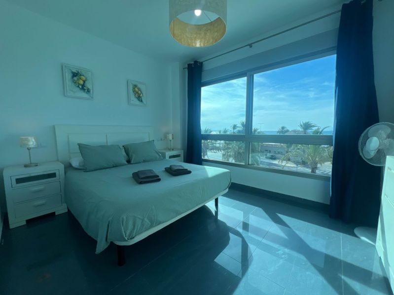 Ložnice rekreačního apartmánu s velkým oknem, postelí a stolky.