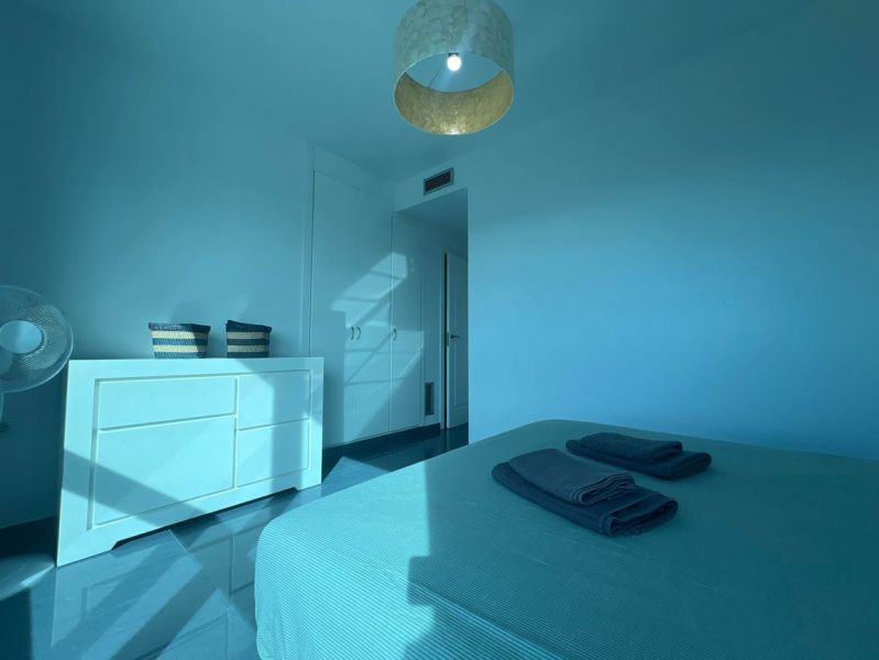 Rekreační apartmán se světlým pokojem, postelí, komodou a lodžií v modrých tónech.