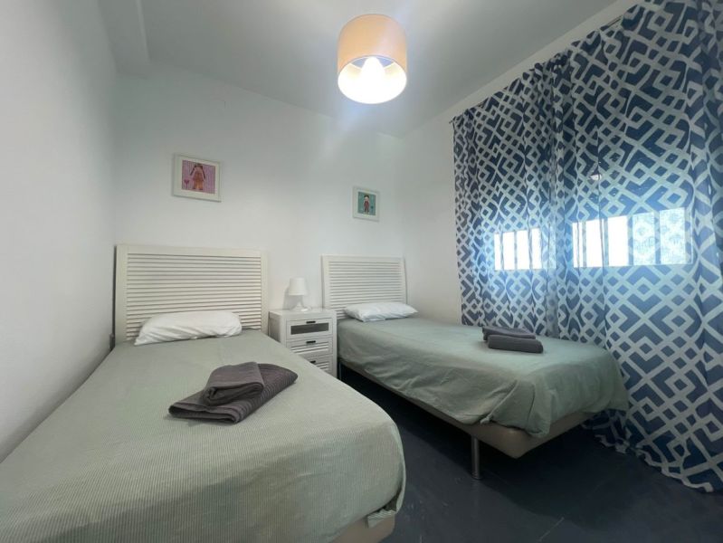 Rekreační apartmán s dvěma jednolůžkovými postelemi, vzorovanými závěsy a stolkem s lampou.