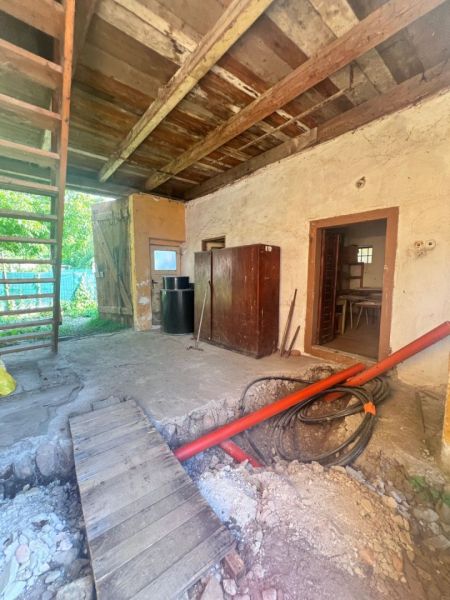 Interiér rodinného domu s dřevěným stropem, rozkopanou podlahou a žebříkem.